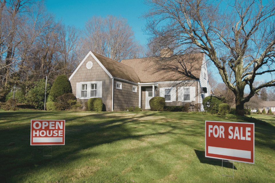 Image shows open house and for sale sign in front of a house