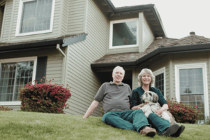 Image shows portrait of a senior couple in front of a house