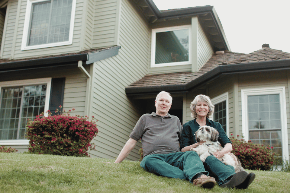 Image shows portrait of a senior couple in front of a house