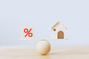 Image shows mortgage rate concept with a wooden home and cube block shape with percent icon on wood scales.
