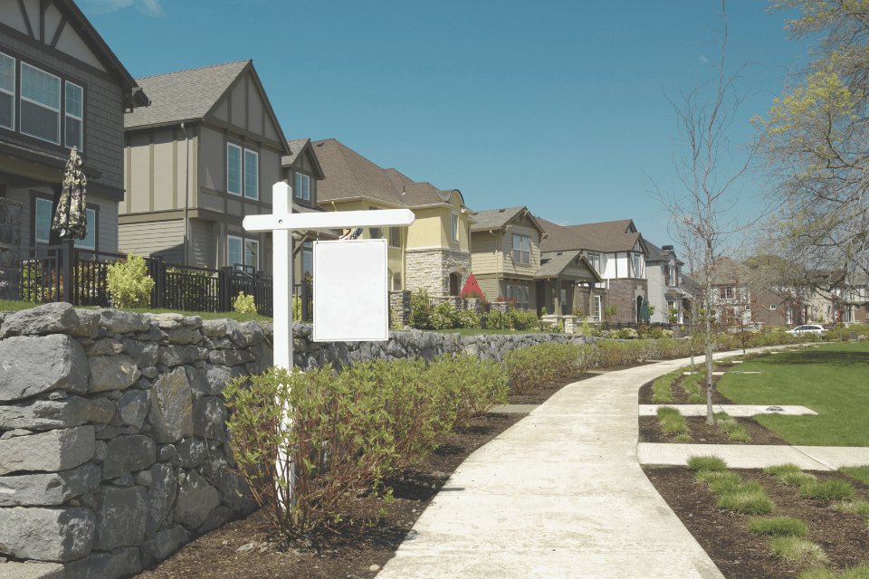 Image shows a row of houses with a For Sale sign in the background