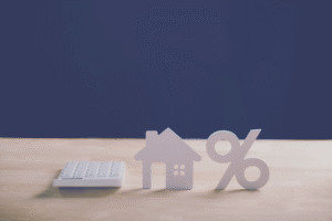 Image shows home property and mortgage rate calculation with wooden house model, percentage sign and calculator for financial planning