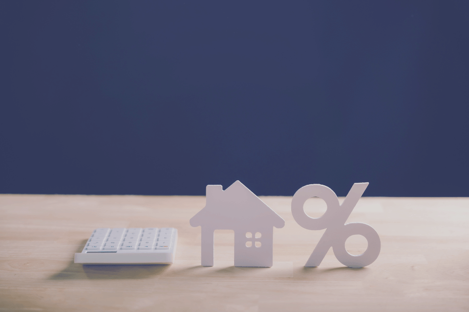 Image shows home property and mortgage rate calculation with wooden house model, percentage sign and calculator for financial planning